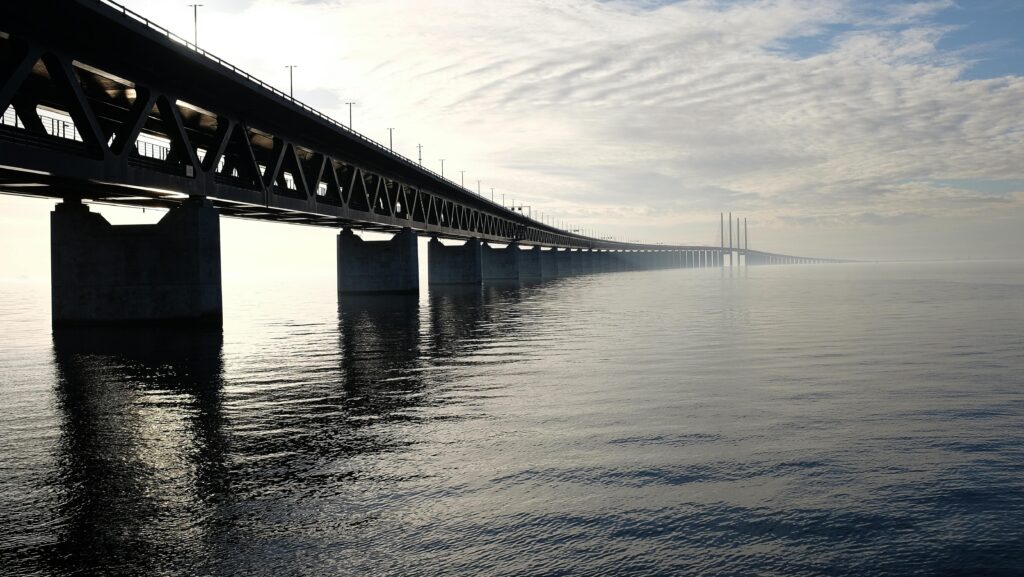 A stunning view of a large steel bridge reflecting on the tranquil water under a cloudy sky.